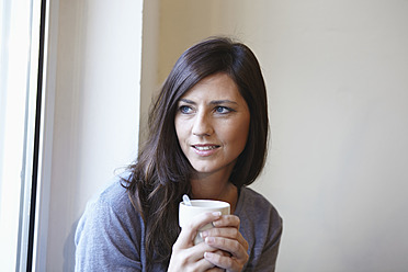 Deutschland, Köln, Mittlere erwachsene Frau am Fenster mit Kaffee, lächelnd - RHF000057