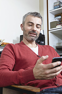 Deutschland, Köln, Älterer Mann sitzt auf Stuhl mit Handy, lächelnd - RHF000067