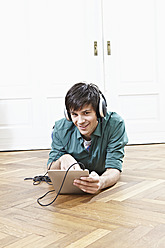 Germany, Cologne, Young man with digital tablet and headphones, smiling, portrait - RHF000074
