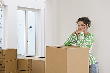 Germany, Bavaria, Grobenzell, Mid adult woman standing near cardboard boxes in house, smiling, portrait - WESTF018086