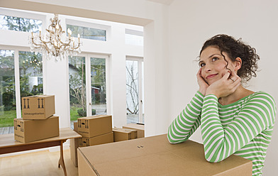 Germany, Bavaria, Grobenzell, Mid adult woman standing near cardboard boxes in house, smiling - WESTF018087