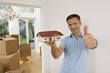 Germany, Bavaria, Grobenzell, Mature man holding model house near cardboard box, smiling, portrait - WESTF018116