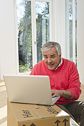 Germany, Bavaria, Grobenzell, Senior man using laptop on cardboard box - WESTF018169