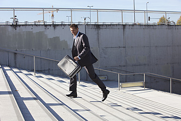 Germany, Bavaria, Munich, Businessman walking on stairs with briefcase, smiling - SKF000710