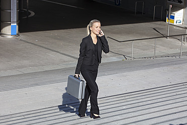 Germany, Bavaria, Munich, Businesswoman on stairs with briefcase and talking on cell phone, smiling - SKF000722