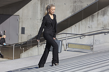 Germany, Bavaria, Munich, Businesswoman walking on stairs with briefcase, smiling - SKF000724