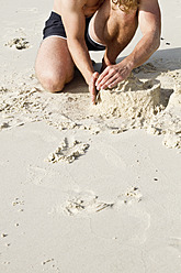 Thailand, Koh Surin, Junger Mann baut Sandburgen am Strand - MBEF000211