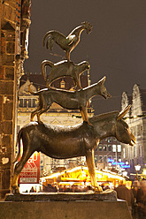 Germany, Bremen, Statue of Bremen City Minstrels in front of Christmas market at night - NDF000230