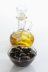 Black olives in glass bowl and bottle of olive oil on white background - CSF015628