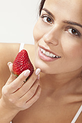 Young woman with strawberry, smiling, portrait - MAEF004109