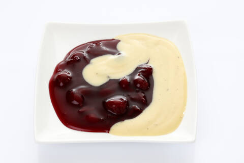 Rote Grütze und Vanillesoße in einem Teller auf weißem Hintergrund, lizenzfreies Stockfoto