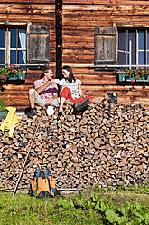 Österreich, Salzburg, Paar sitzt auf Baumstämmen bei Hütte - HHF003799