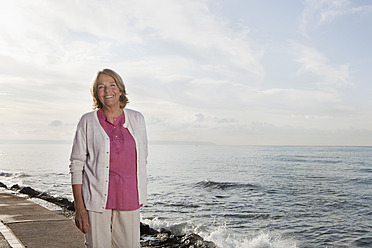 Spain, Mallorca, Senior woman standing at sea shore, smiling, portrait - SKF000764