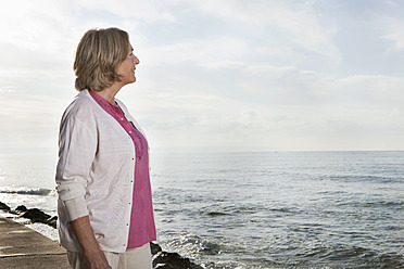 Spain, Mallorca, Senior woman standing at sea shore, smiling - SKF000766
