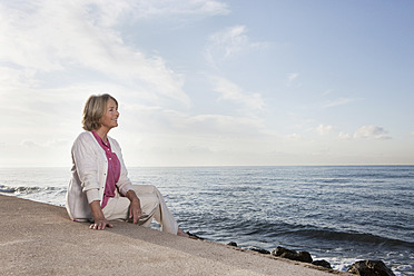 Spain, Mallorca, Senior woman sitting at sea shore, smiling - SKF000769