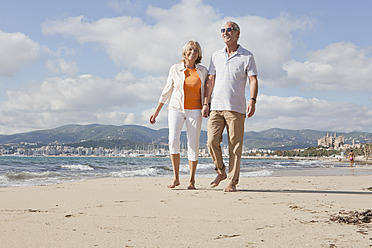 Spain, Mallorca, Senior couple walking along beach, smiling - SKF000830
