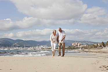 Spain, Mallorca, Senior couple walking along beach, smiling - SKF000831