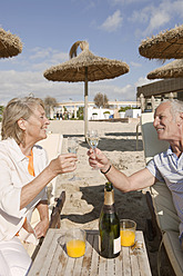 Spain, Mallorca, Senior couple drinking sparkling wine at beach - SKF000859