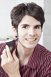 Junger Mann beim Rasieren mit Elektrorasierer, Porträt - MAEF004234