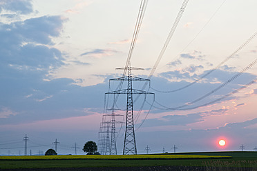 Germany, Bavaria, View of electricity pylon in rapeseed field at sunset - FOF003868