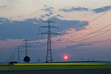 Germany, Bavaria, View of electricity pylon in rapeseed field at sunset - FOF003869