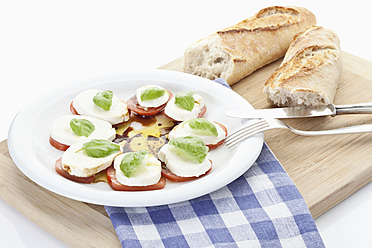 Mozzarella, Brot, Tomatenscheiben mit Basilikum auf Schneidebrett - MAEF004300