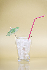 Zuckerwürfel im Glas mit Strohhalm und Cocktailschirmchen auf cremefarbenem Hintergrund - ANBF000010