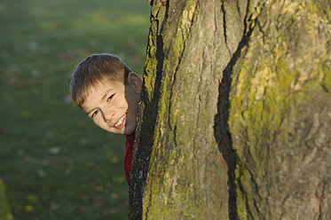 Germany, Bavaria, Boy standing behind tree trunk, portrait - RUEF000841
