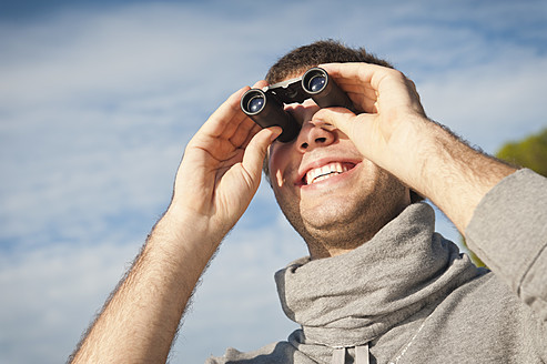 Spain, Mallorca, Young man looking through binocular, smiling - MFPF000018