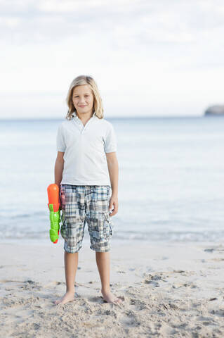 Spanien, Mallorca, Junge mit Wasserpistole am Strand, Porträt, lizenzfreies Stockfoto