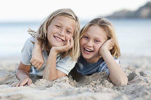 Spanien, Mallorca, Kinder liegen im Sand am Strand, lächelnd, Porträt - MFPF000095