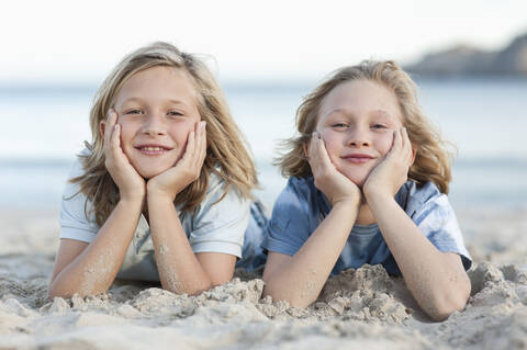 Spanien, Mallorca, Kinder liegen im Sand am Strand, lächelnd, Porträt, lizenzfreies Stockfoto