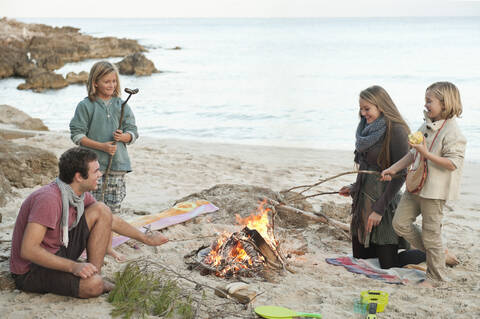 Spanien, Mallorca, Freunde grillen Würstchen am Lagerfeuer am Strand, lizenzfreies Stockfoto