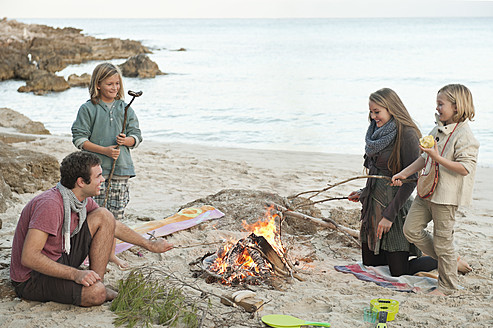 Spain, Mallorca, Friends grilling sausages at camp fire on beach - MFPF000107