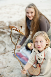 Spain, Mallorca, Friends looking at grilled sausage on beach - MFPF000110