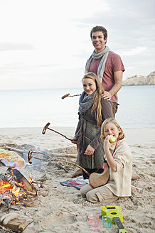 Spain, Mallorca, Friends with sausages at camp fire on beach - MFPF000111