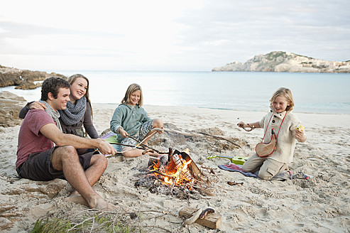 Spain, Mallorca, Friends grilling sausages at camp fire on beach - MFPF000113