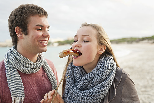 Spain, Mallorca, Young man feeding grilled sausage to teenage girl - MFPF000115