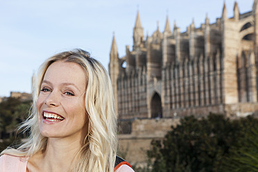 Spanien, Mallorca, Palma, Junge Frau stehend mit der Kathedrale St. Maria im Hintergrund, lächelnd - SKF000872