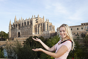 Spanien, Mallorca, Palma, Junge Frau stehend mit Kathedrale Santa Maria im Hintergrund, lächelnd, Porträt - SKF000874