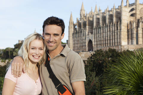 Spanien, Mallorca, Palma, Paar stehend mit Kathedrale Santa Maria im Hintergrund, lächelnd, Porträt, lizenzfreies Stockfoto