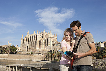 Spanien, Mallorca, Palma, Pärchen schaut in Reiseführer mit Kathedrale St. Maria im Hintergrund, lächelnd - SKF000883