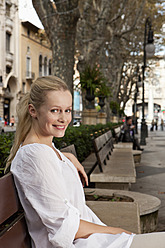 Spain, Mallorca, Palma, Young woman sitting on bench, smiling, portrait - SKF000911