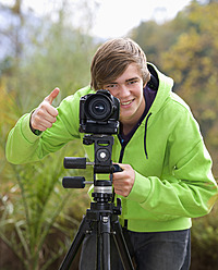 Austria, Young man with camera, smiling, portrait - WWF002090
