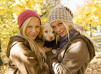 Österreich, Schwestern halten Hund im Herbst, lächelnd, Porträt - WWF002330
