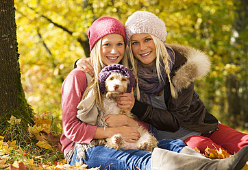 Austria, Sisters sitting with dog in autumn, smiling, portrait - WWF002158