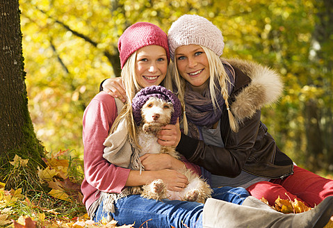 Österreich, Schwestern sitzend mit Hund im Herbst, lächelnd, Porträt - WWF002158