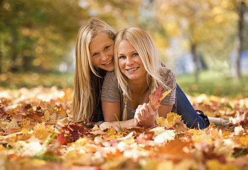 Austria, Sisters lying on autumn leaf, smiling, portrait - WWF002172