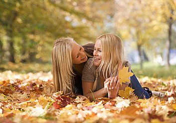 Austria, Sisters lying on autumn leaf, smiling - WWF002173