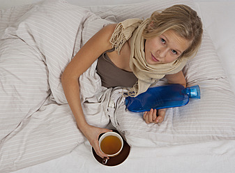 Teenage girl lying on bed with hot water bottle and tea cup - WWF002199